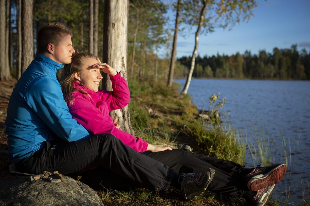 Nuoripari istuu sylikkäin järven rannalla ja katsoo horisonttiin.